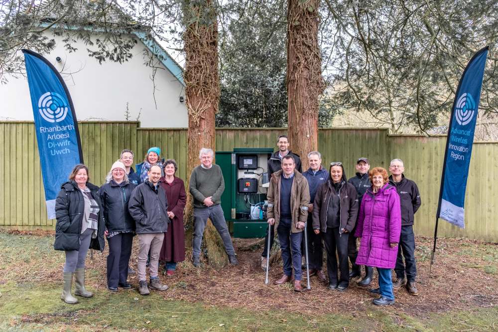 Group of stakeholders standing beside a Meteor water quality monitoring kiosk in Ludlow.
